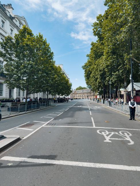A Brompton Movers vehicle is parked on a city street outside a row of historic and modern buildings, with a loading area in front of an entrance featuring a white stone gate and columns. The vehicle, 