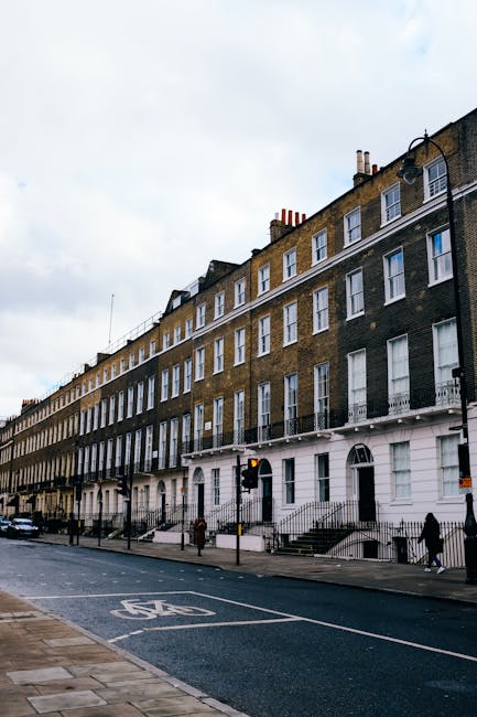 Exterior view of a row of Victorian-style terraced houses in the SW3 postcode area, featuring white facades, decorative columns, and black wrought iron balconies. The street has parked cars along the 